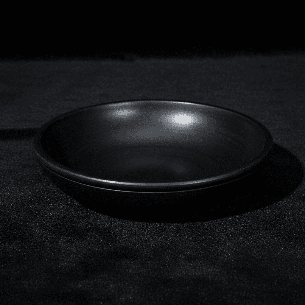 A high-resolution studio shot of the Black Stone Scrying Bowl, 6 Inch, positioned centrally on a sleek, dark velvet cloth backdrop to emphasize its matte black, slightly textured surface. The scene is illuminated with softbox lighting to create gentle, eve