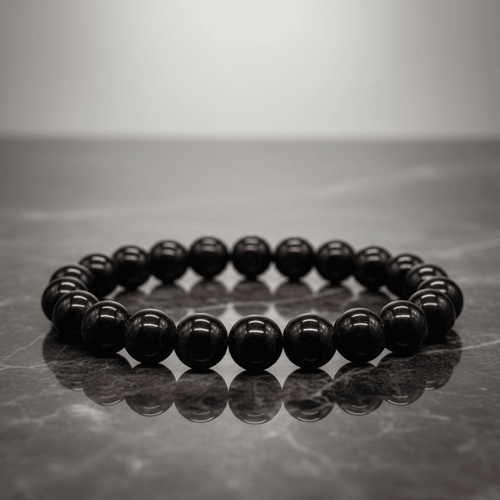A close-up shot of the Jet Gemstone Bracelet, 8mm beads, elegantly displayed on a reflective dark marble surface under softbox lighting that enhances the smooth, glossy texture of the jet stones. The camera angle is straight-on with a focus on the uniformi