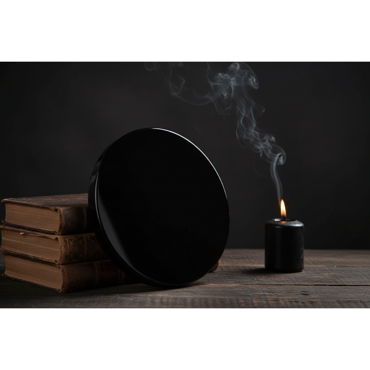 Black Obsidian Scrying Mirror 8 inch propped upright against leather books with black candle