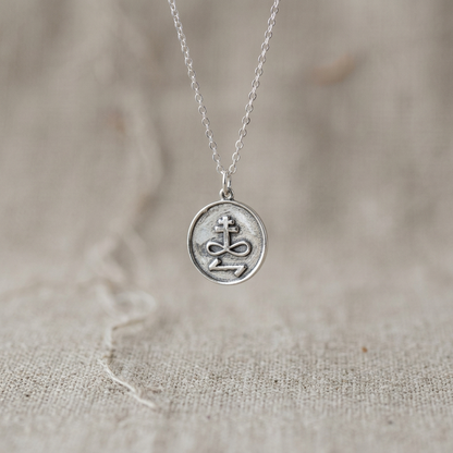 Detailed close-up of small silver Destroy Enemies talisman hanging from minimalist chain against neutral fabric background, emphasizing craftsmanship.