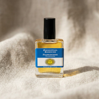 Close-up of 1/2 oz frankincense perfume oil bottle by Escential Essences on textured beige fabric, highlighting amber oil and glass details.