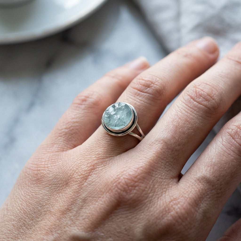 Close-up of petite aquamarine ring on smooth marble surface highlighting silver band and gemstone glow.