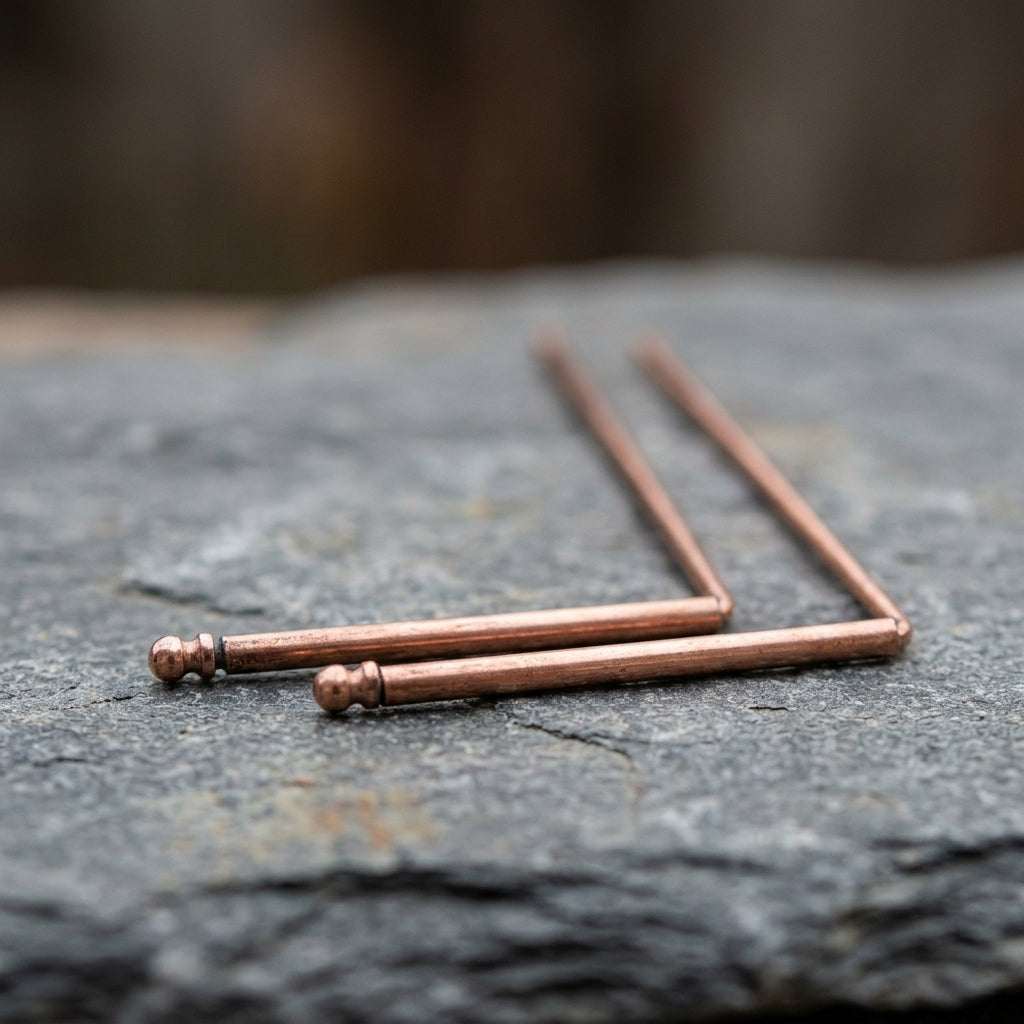 Close-up of copper dowsing rods on natural stone, highlighting warm tones and micro-texture details.