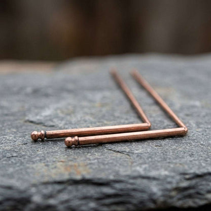 Close-up of copper dowsing rods on natural stone, highlighting warm tones and micro-texture details.