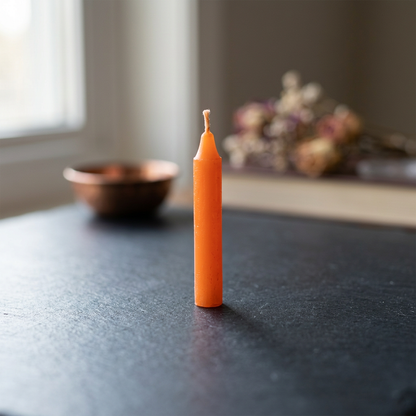 Close-up shot of a single 6-inch orange candle revealing micro-texture of wax surface and steady wick, set on a dark natural lit surface.