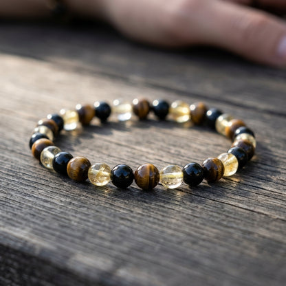 Close-up of a 6mm tiger's eye, citrine, and black tourmaline protection bracelet on a wooden surface, highlighting bead details.