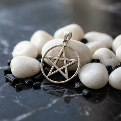 Miniature sterling silver pentagram pendant nestled among white stones on dark marble, emphasizing delicate symbol details.