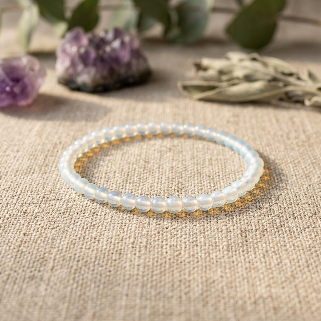 Opalite bracelet, 4mm, placed on linen fabric with a soft focus, illuminated by warm light, and surrounded by crystals and foliage for a spiritual ambiance.
