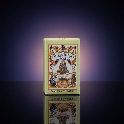 A close-up shot of the Florida Water Soap 95 grams placed on a reflective black surface in a sophisticated professional studio. The scene is lit with softbox lighting to create a smooth, even glow that highlights the soap's textured, slightly glossy surfac