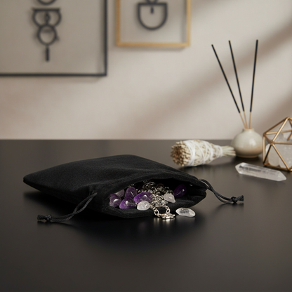 A high-resolution, studio shot of a Black Velveteen Pouch measuring 5 x 7 inches, placed on a sleek, matte black surface within a modern, minimalistic metaphysical home setting. The scene is lit with softbox lighting from above, creating gentle shadows and