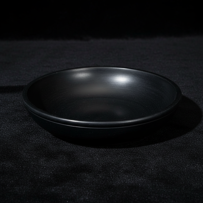 A high-resolution studio shot of the Black Stone Scrying Bowl, 6 Inch, positioned centrally on a sleek, dark velvet cloth backdrop to emphasize its matte black, slightly textured surface. The scene is illuminated with softbox lighting to create gentle, eve
