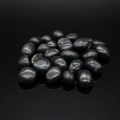 Capture a close-up, high-resolution image of a pile of Agni Manitite Tumbled Stones, 1 lb, 20-22mm diameter, spread out naturally on a sleek, reflective black surface. Use HDR studio lighting with soft diffused daylight balance to highlight the smooth, rou