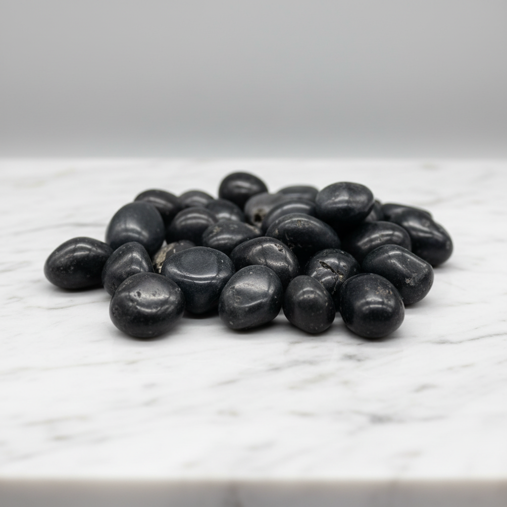 Present a professional studio environment with a minimalist aesthetic: Agni Manitite Tumbled Stones neatly arranged on a pristine white marble slab with subtle natural veining. Employ softbox lighting softened with diffusion to evenly illuminate the stones