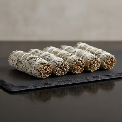 Capture a high-resolution, professional studio shot of a set of six white sage smudge sticks arranged elegantly on a dark, matte surface to emphasize their natural textures and organic form. Use softbox lighting to create gentle, diffused light that highli