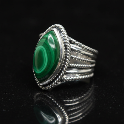 Capture a close-up, product-focused shot of the size 12 Malachite Marquise Ring, positioned elegantly on a reflective black velvet surface to emphasize its intricate craftsmanship and polished surface. Use diffused daylight studio lighting to create soft s