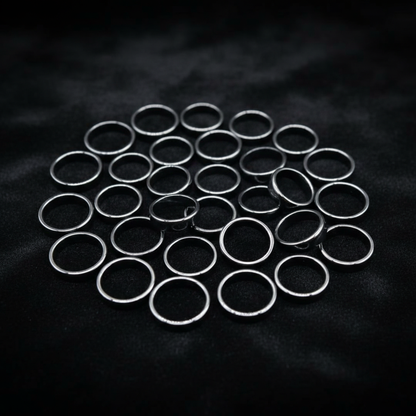 Create a highly detailed, studio-quality image of a set of 50 flat hematite rings displayed on an elegant, dark velvet fabric surface, under softbox lighting that highlights the smooth, matte textures of the stones. The rings are arranged in a circular for