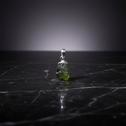 Craft a dramatic, cinematic shot of a Moldavite pendant lying on a polished, dark marble surface, illuminated by HDR studio lighting to bring out the vibrant, organic texture of the stone. The pendant, approximately 0.5 inches in length, is displayed promi