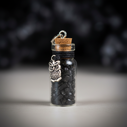 Create a high-resolution, studio shot of the black Tourmaline chips in a transparent glass bottle, captured from a slight angle to showcase the tiny chips inside. Utilize a softbox lighting setup to create even, diffused light, highlighting the natural tex