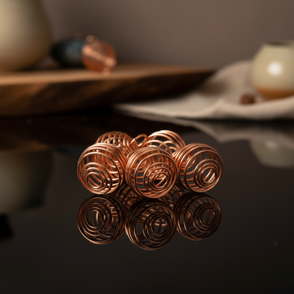 Create a highly detailed, professional studio shot of a set of 24 copper-plated coils arranged artistically on a sleek, reflective black surface. Use softbox lighting to emphasize the warm, rich tones of the copper with gentle highlights on the spiraling c