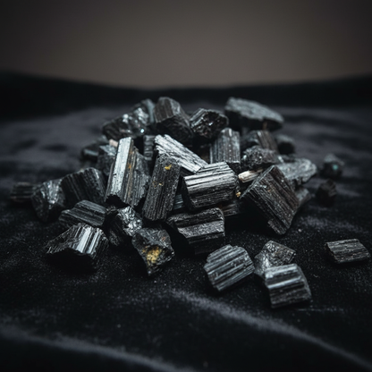 Create a highly detailed, cinematic studio shot of a handful of Black Tourmaline Untumbled Stones, positioned on a sleek black velvet surface, illuminated by softbox lighting that highlights their natural, matte textures and rough, unpolished surfaces. Cap