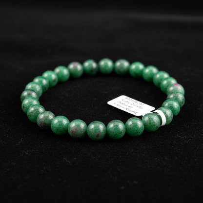 A luxurious macro shot of a Ruby Zoisite bracelet with 5mm to 8mm beads, elegantly draped over a smooth, reflective black velvet surface. The scene is illuminated with HDR studio lighting using softboxes to create even, diffused daylight, highlighting the 