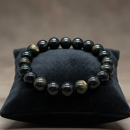 Create a high-end, cinematic studio shot of the Goldsheen Obsidian Bracelet, 8mm size, featuring a close-up front view with a focus on the gleaming metallic sheen and smooth, polished surface of the beads. Use softbox lighting with a slight rim light to ac