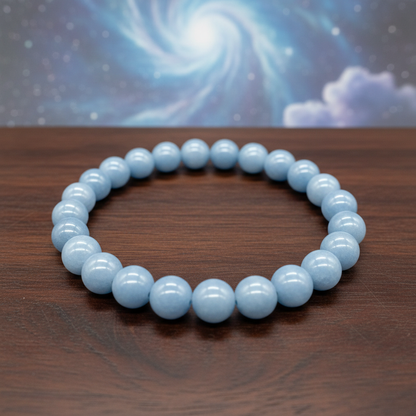 Capture a close-up, top-down shot of the Angelite Bead Bracelet, 8mm, resting on a polished dark wooden surface that enhances its soothing blue-gray hues. Use softbox lighting to create gentle, diffuse daylight that highlights the smooth, matte texture of 