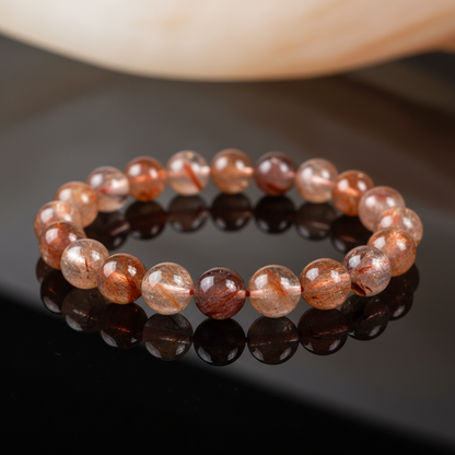 Create a hyper-realistic, studio-shot image of the Himalayan Fire Quartz Beaded Bracelet, featuring 6-8mm beads intricately arranged on a sleek, reflective black surface. Use HDR studio lighting with a softbox to highlight the fiery inclusions within each 