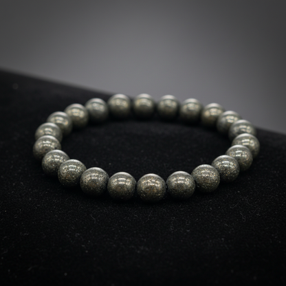 Capture a close-up, macro shot of the Pyrite Beaded Bracelet with 8mm beads glistening under soft HDR studio lighting. Use a shallow depth of field with a focus on the intricate, metallic luster of each bead, highlighting their fool's gold appearance. The 