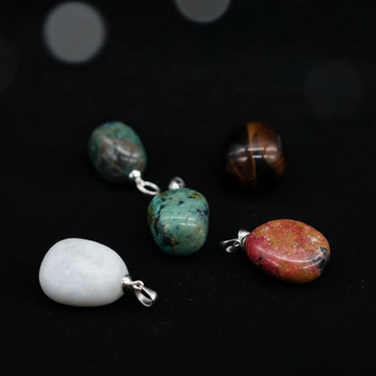 Create a highly detailed close-up studio shot of a collection of ~3/4' tumbled stone pendants, each with unique irregular shapes and textured surfaces, elegantly displayed against a sleek, dark velvet backdrop. Use softbox lighting from the side to accentu