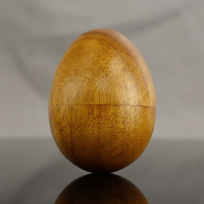 Capture a high-resolution, studio shot of the Wooden Egg Shaker, measuring 2 3/4 x 2 inches, illuminated with a softbox lighting setup that emphasizes its smooth, polished wooden surface and subtle grain texture. Use a macro lens with a shallow depth of fi