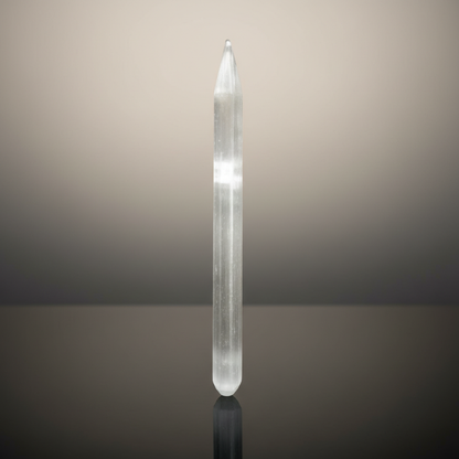 Create a stunning, cinematic studio shot of a white selenite wand, positioned vertically on a glossy black reflective surface that emphasizes its luminous, translucent qualities. The scene is illuminated with softbox lighting to create a gentle, even glow 