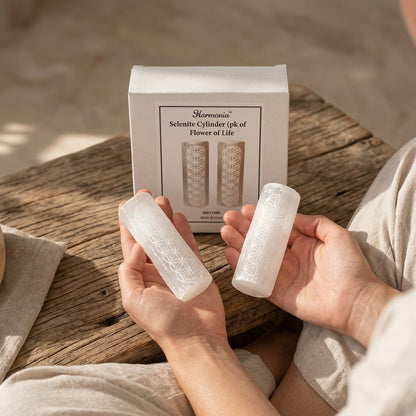 Balanced pair of 4-inch selenite harmonizers held in hands on wooden surface in a calming meditation space with natural light.