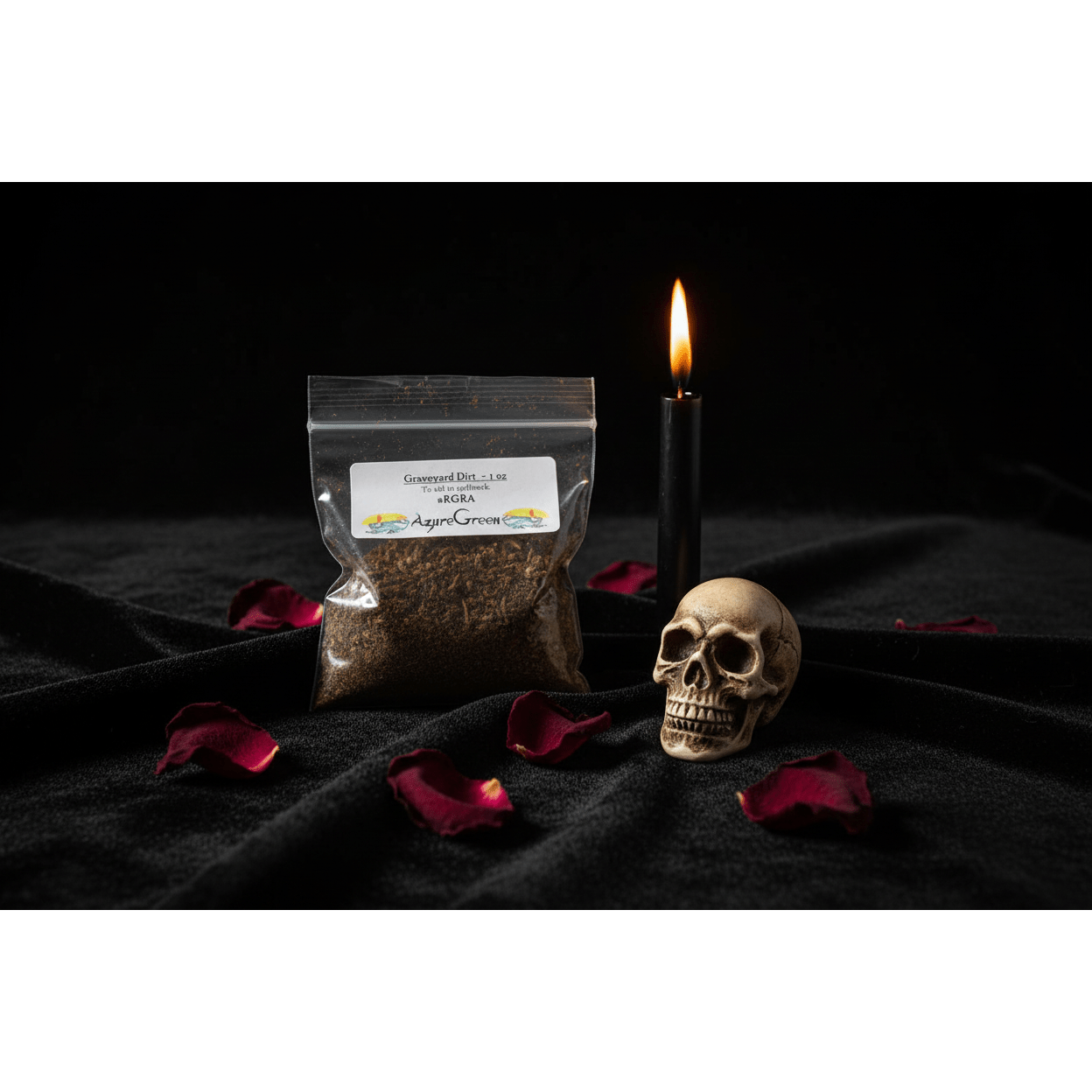 1oz resealable bag of graveyard dirt on black velvet cloth with a burning black taper candle, skull figurine, and dried rose petals