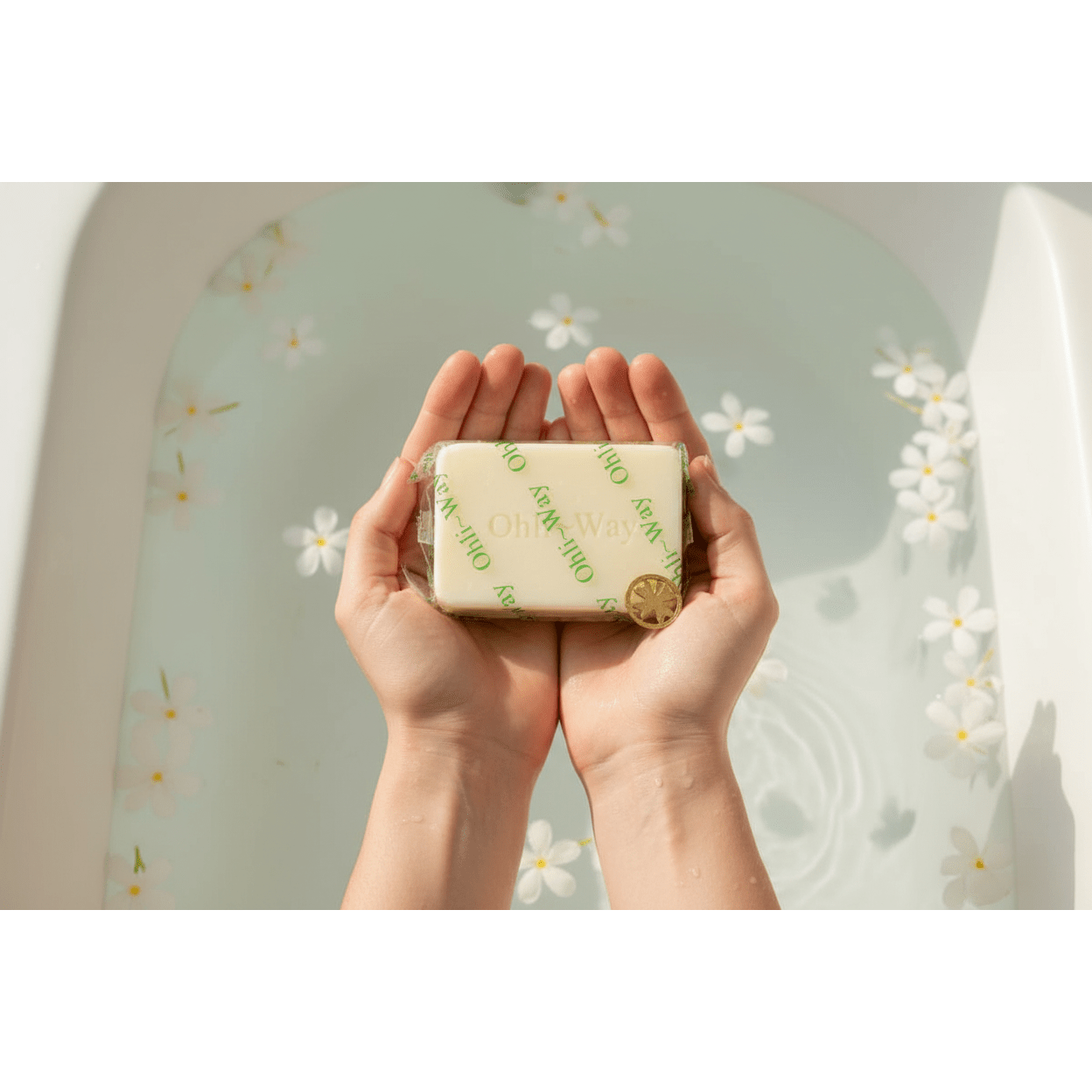 Ohli~Way Coconut Spiritual Cleansing Soap 100g bar held in cupped hands over a petal-filled white ceramic bathtub