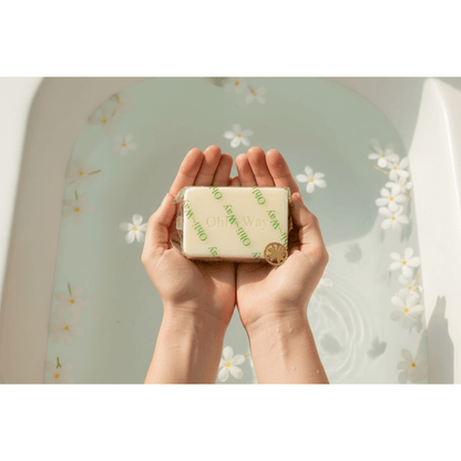 Ohli~Way Coconut Spiritual Cleansing Soap 100g bar held in cupped hands over a petal-filled white ceramic bathtub