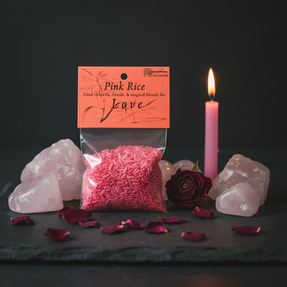 1oz Pink Infused Love Rice bag on a dark slate altar with rose quartz crystals, lit pink taper candle, and dried rose petals