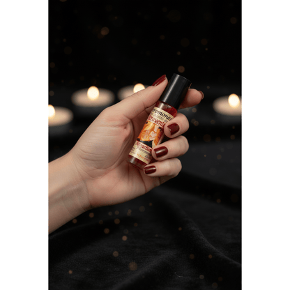Hand holding Attraction Perfume Oil roll-on bottle ready to apply, dark velvet background with bokeh candlelight