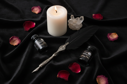 Steampunk calligraphy pen and ink bottles on black velvet with rose petals, candle, and crystal