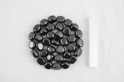 Hematite magnetic tumbled stones arranged in a crystal grid on white linen with selenite wand