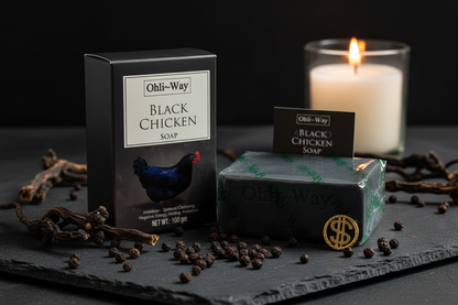 Ohli-Way Black Chicken Soap box, wrapped bar, insert card, and gold coin charm on dark slate with peppercorns and candlelight