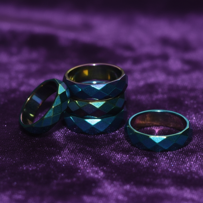 Macro close-up of rainbow magnetic hematite faceted rings on dark velvet showing iridescent rainbow shimmer