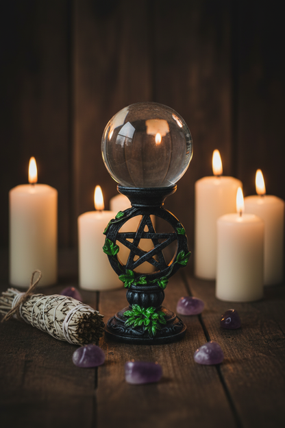 Clear crystal gazing ball on pentagram stand on a candlelit altar with sage and amethyst