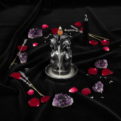 Overhead flat lay of Maiden, Mother, Crone backflow incense burner with amethyst, lavender, and candle on black velvet