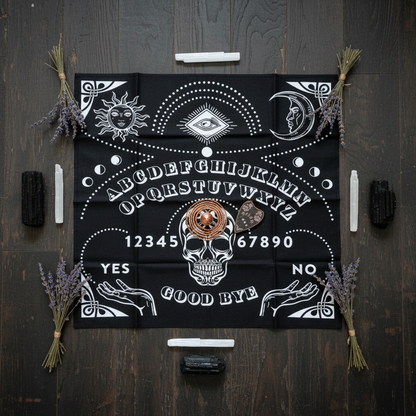 Overhead flat-lay of Ouija Board Mat on dark wood floor with a copper pendulum, black tourmaline, lavender, and selenite wand