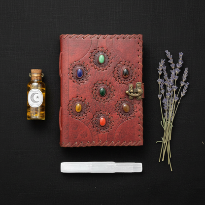 7 Chakra Leather Journal flat lay on black linen with ritual oil bottle, lavender sprigs, and selenite wand