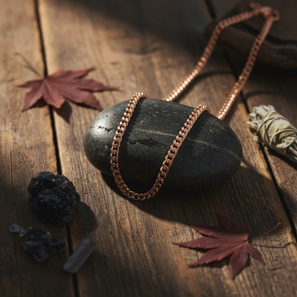 Copper heavy chain necklace draped over a smooth dark stone on a wooden surface with warm earthy tones