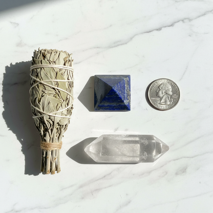 Lapis lazuli crystal pyramid, 1 inch wide, flat lay on white marble with sage and quartz