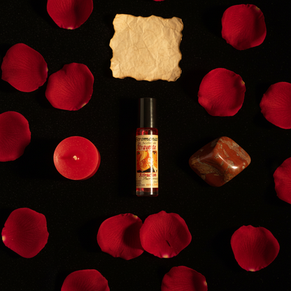 Flat lay of Attraction Perfume Oil roll-on bottle on black velvet with rose petals, red candle, and red jasper crystal
