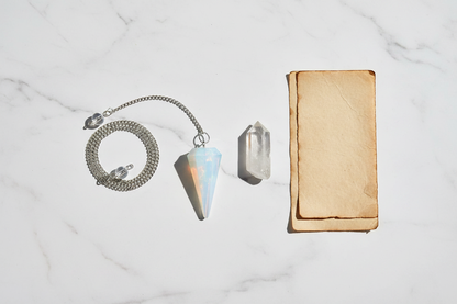 6-sided opalite pendulum on white marble with clear quartz point and parchment